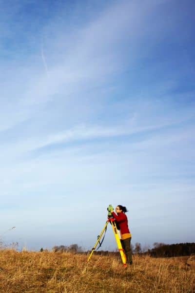 Land surveyor fieldwork daylight - ALTA SURVEY Idaho Licensed land surveyor adjusting a total station on a tripod during fieldwork, representing accuracy steps in an ALTA Land Title Survey.