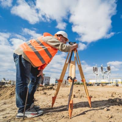 Surveyor using field equipment to confirm site measurements for an alta land title survey before a lender closing