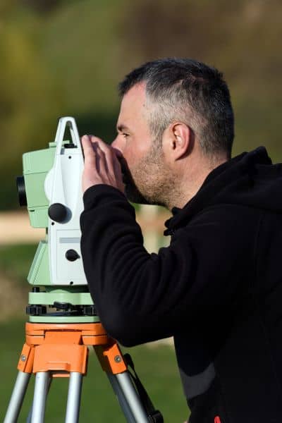 Land surveyor using equipment to check property lines during an alta title survey
