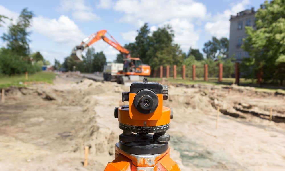 Alta title survey road project pause - ALTA SURVEY Idaho Surveying instrument focused on a paused road construction site with an excavator in the background representing how road delays impact an alta title survey
