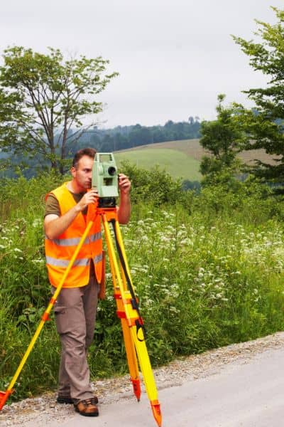 Land surveyor using equipment to measure a roadside property during an ALTA land title survey