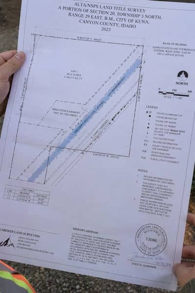A surveyor using a tablet and GPS equipment while standing near open land, reviewing property boundaries and irrigation easements as part of an alta land survey process before land development
