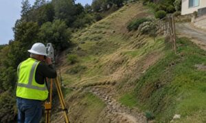 Land surveyor collecting topographic data on a hillside before retaining wall planning