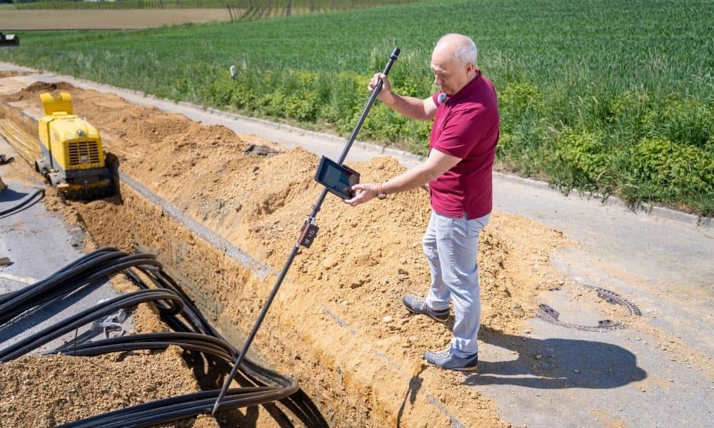 Surveyor performing a construction survey beside a utility trench while checking site measurements before excavation